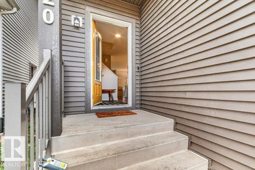 Concrete entry steps with a wood-finish railing, leading to a yellow front door with a window pane - 1020 Daniels Loop Sw, Edmonton, AB 