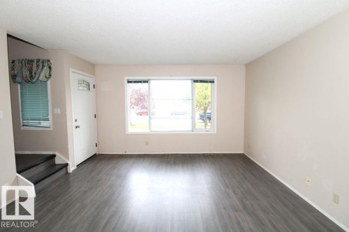 Gray wood-finish flooring, white entry door with decorative glass, and a neutral wall color throughout - 11393 22 Avenue Nw, Edmonton, AB 