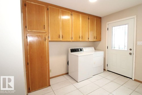 Extensive wood-finish cabinetry, white tile flooring, and a white exterior door with glass paneling - 11393 22 Avenue Nw, Edmonton, AB 