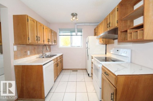 Galley kitchen featuring wood-finish cabinetry, white countertops, tile flooring, and a stainless steel double basin sink - 11393 22 Avenue Nw, Edmonton, AB 