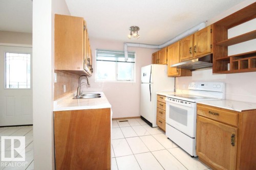 Kitchen featuring wood cabinetry, white appliances, white tile flooring, and a double basin sink - 11393 22 Avenue Nw, Edmonton, AB 