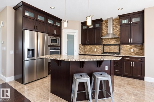 Kitchen featuring dark wood cabinetry, stainless steel appliances, a center island with a light-toned countertop, and a tiled backsplash - 258 Albany Drive Nw, Edmonton, AB 