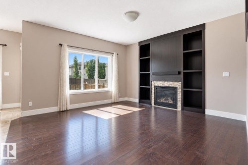 Rich wood-finish flooring, built-in shelving, stone-surround fireplace, large window, and recessed lighting - 258 Albany Drive Nw, Edmonton, AB 
