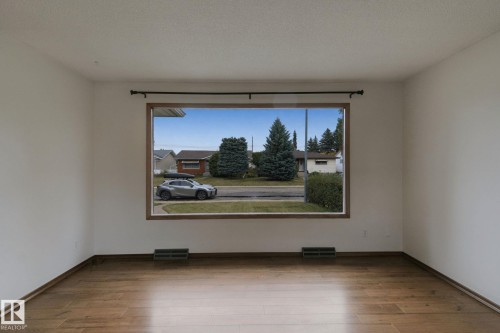 Spacious room featuring wood-finish flooring, white painted walls, and a large window with wood-trim framing - 8424 70 Street Nw, Edmonton, AB 