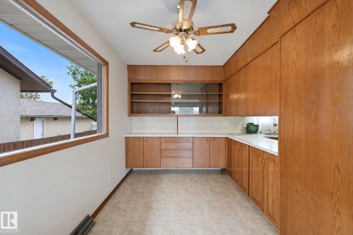 Built-in wood-finish cabinetry, neutral flooring, white countertops, textured backsplash, and a window for natural light - 8424 70 Street Nw, Edmonton, AB 