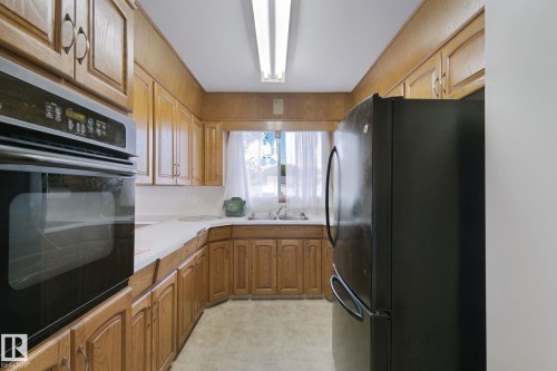 Galley kitchen featuring wood cabinetry, white countertops, a built-in oven, and a black refrigerator - 8424 70 Street Nw, Edmonton, AB 