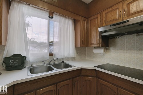 Wood-finish cabinetry with brass-tone hardware, a double basin stainless steel sink, and a built-in cooktop - 8424 70 Street Nw, Edmonton, AB 