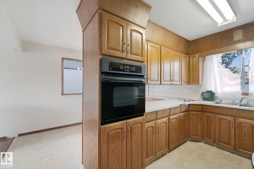 Wood-finish cabinetry, built-in oven, white countertops, and a double-basin sink - 8424 70 Street Nw, Edmonton, AB 