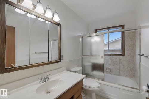Bathroom featuring a vanity with an integrated sink, tri-fold mirrored medicine cabinet, overhead lighting, and a bathtub with a sliding glass enclosure - 8424 70 Street Nw, Edmonton, AB 