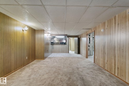 Wood-finish wall paneling, wall-mounted light fixtures, textured carpet, drop ceiling, and interior doorways - 8424 70 Street Nw, Edmonton, AB 