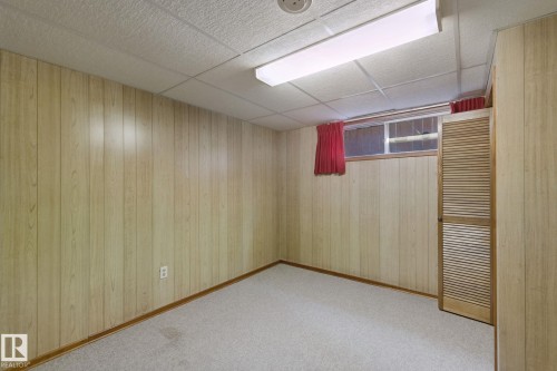 Textured drop ceiling, fluorescent lighting fixture, wood-finish wall paneling, window with glass panes, and louvered bifold door - 8424 70 Street Nw, Edmonton, AB 