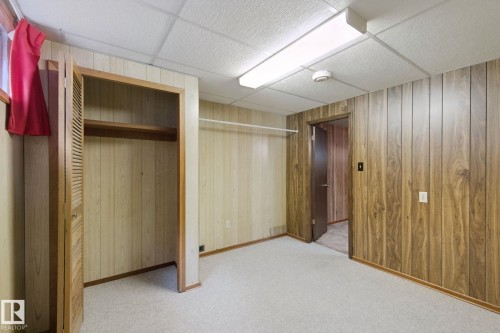 Wood-panel walls, drop ceiling with fluorescent lighting, light-colored carpet, and an open closet with a built-in shelf and hanging rod - 8424 70 Street Nw, Edmonton, AB 