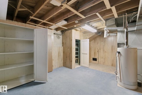 Unfinished basement featuring exposed wood ceiling joists, light wood-paneled walls, and built-in white shelving - 8424 70 Street Nw, Edmonton, AB 