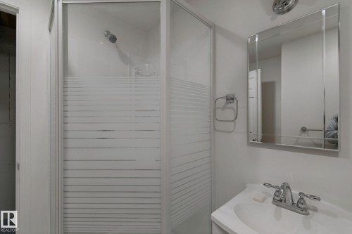 Enclosed shower with frosted glass, wall-mounted shower head, single-basin vanity, chrome faucet, and mirrored medicine cabinet - 8424 70 Street Nw, Edmonton, AB 