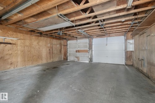 Concrete flooring, plywood wall panels, exposed wood ceiling joists, and two overhead garage doors - 8424 70 Street Nw, Edmonton, AB 