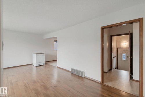 Hardwood flooring, painted white walls, wood-trimmed doorway, white dishwasher, paneled entry door with decorative glass - 8424 70 Street Nw, Edmonton, AB 