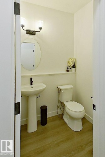 Pedestal sink with a matte black faucet, oval mirror, wall-mounted vanity lighting, and wood-finish flooring - 40 Jamison Crescent, St. Albert, AB 