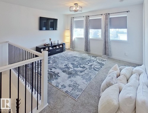 Carpeted upper-level space featuring a contemporary chandelier, white walls, and three windows with roller shades - 40 Jamison Crescent, St. Albert, AB 