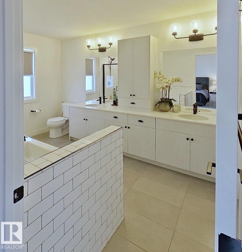 White subway tile partial wall, dual vanity with undermount sinks, white cabinetry, dark bronze hardware, and tile flooring - 40 Jamison Crescent, St. Albert, AB 