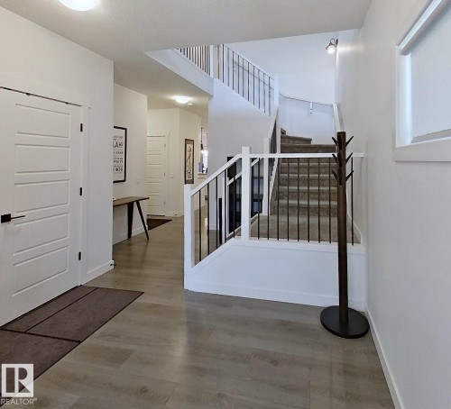 Multi-level entryway featuring wood-finish flooring, white walls, and a staircase with carpeted treads and black metal railings - 40 Jamison Crescent, St. Albert, AB 