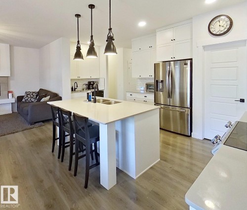 Modern kitchen with wood-finish flooring, white cabinetry, stainless steel appliances, and a central island featuring a double sink - 40 Jamison Crescent, St. Albert, AB 