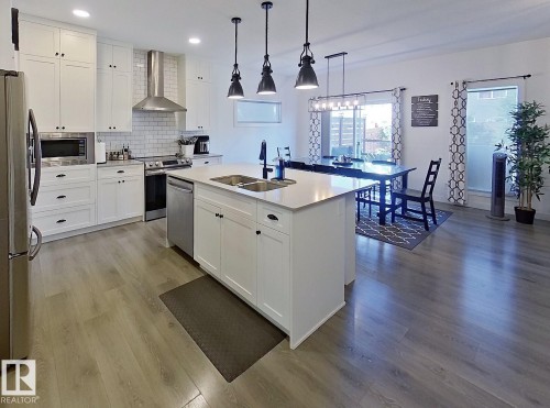Open-concept kitchen with white shaker cabinetry, stainless steel appliances, a center island with double sink, and wood-finish flooring - 40 Jamison Crescent, St. Albert, AB 