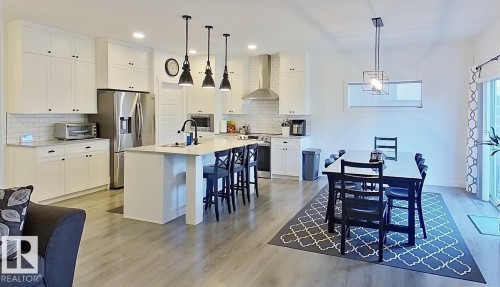 Open-concept kitchen and dining area featuring light wood-finish flooring, white cabinetry, a large kitchen island with pendant lighting, stainless steel appliances, and a subway tile backsplash - 40 Jamison Crescent, St. Albert, AB 