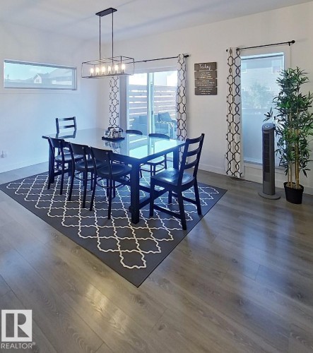 Wood-finish flooring throughout, complemented by a large sliding glass door, a horizontal transom window, and a modern rectangular chandelier - 40 Jamison Crescent, St. Albert, AB 