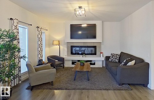 Integrated electric fireplace with tiled surround, wood-finish flooring, two large windows, recessed lighting, and a modern ceiling fixture - 40 Jamison Crescent, St. Albert, AB 