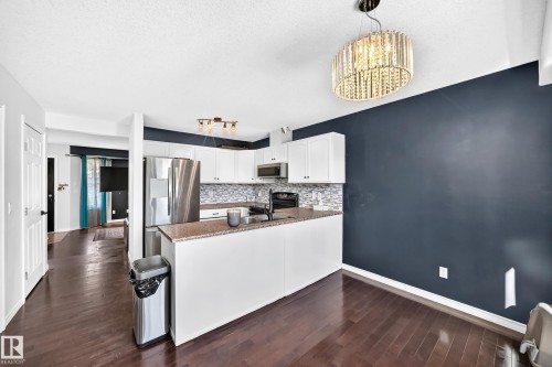 Kitchen featuring wood-finish flooring, white cabinetry, a mosaic tile backsplash, and stainless steel appliances - 447 Songhurst Place, Leduc, AB 