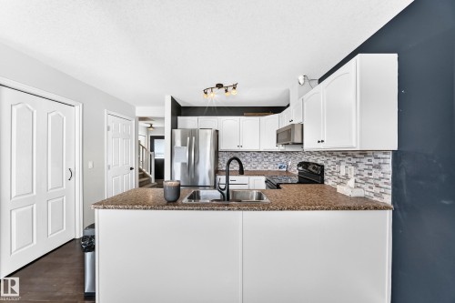 White cabinetry with matte black hardware, stainless steel appliances, mosaic tile backsplash, and a double basin sink with a matte black faucet - 447 Songhurst Place, Leduc, AB 