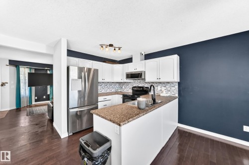 White cabinetry with dark hardware, stainless steel refrigerator, patterned tile backsplash, dark wood-finish flooring, and a counter with an integrated sink - 447 Songhurst Place, Leduc, AB 