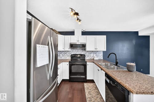 Stainless steel refrigerator, white cabinetry, dark wood-finish flooring, dual basin stainless steel sink, and a black range - 447 Songhurst Place, Leduc, AB 
