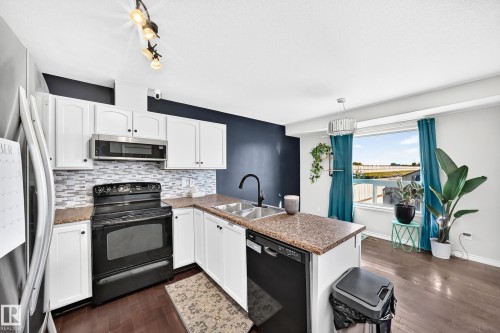 Kitchen featuring white cabinetry, a mosaic tile backsplash, wood-finish flooring, and a window - 447 Songhurst Place, Leduc, AB 