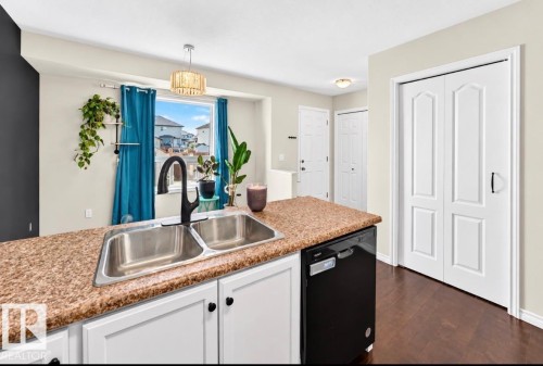 Kitchen island featuring a double basin stainless steel sink, black gooseneck faucet, and integrated black dishwasher - 447 Songhurst Place, Leduc, AB 