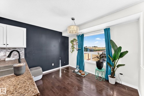 Hardwood-finish flooring with a large window, white cabinetry, and a stone-finish countertop - 447 Songhurst Place, Leduc, AB 