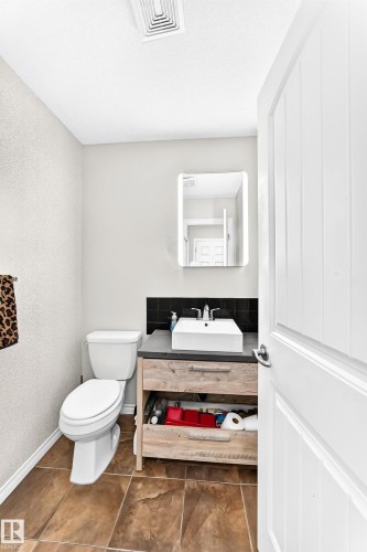 Modern vanity with an integrated vessel sink, wood-finish cabinetry, and a dark countertop - 447 Songhurst Place, Leduc, AB 