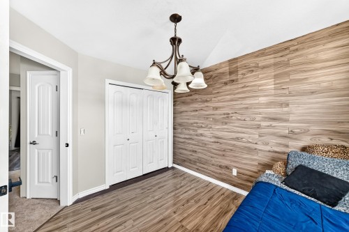 Vaulted ceiling with a chandelier, wood-finish accent wall, wood-finish flooring, and bi-fold closet doors - 447 Songhurst Place, Leduc, AB 