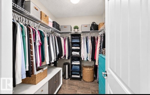 Walk-in closet featuring wire shelving, multiple hanging rods, built-in drawer storage, and wood-finish flooring - 447 Songhurst Place, Leduc, AB 