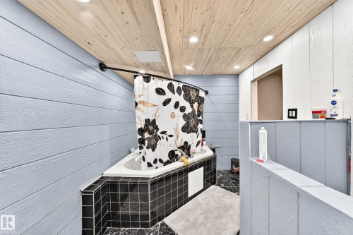 Corner soaking tub with black tile surround, wood-finish plank ceiling, recessed lighting, and wall paneling - 447 Songhurst Place, Leduc, AB 