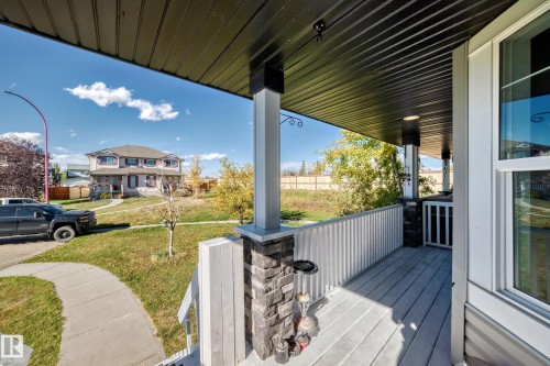 Front porch with composite decking, decorative stone pillar accents, and a black soffit ceiling - 447 Songhurst Place, Leduc, AB 