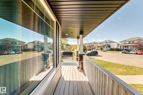 Covered porch featuring wood-finish decking, stone-clad pillars, and a white railing - 447 Songhurst Place, Leduc, AB 