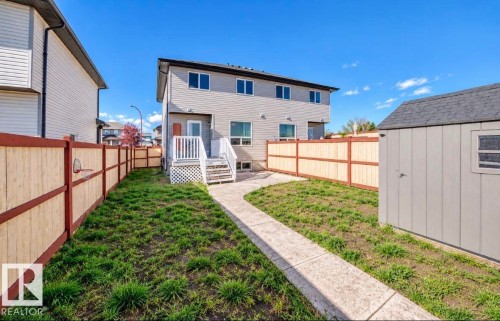 Fenced yard featuring a concrete pathway, rear deck with stairs, and a detached storage shed - 447 Songhurst Place, Leduc, AB 