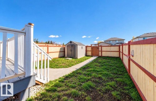 Expansive backyard featuring a concrete pathway, a storage shed, wood fencing with a gate, and a composite deck - 447 Songhurst Place, Leduc, AB 
