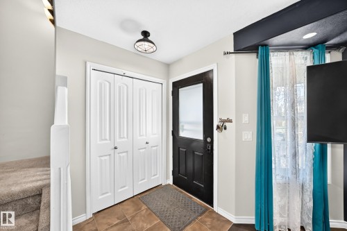 Entryway featuring a dark-toned door with frosted glass, tiled flooring, white bi-fold closet doors, and recessed lighting - 447 Songhurst Place, Leduc, AB 