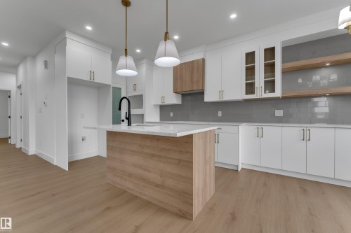 Kitchen featuring white cabinetry, a wood-finish island, solid surface countertops, and a subway tile backsplash - 178 Munn Way, Leduc, AB 
