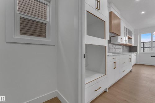 White custom cabinetry with integrated appliance spaces, gold-tone hardware, wood-finish flooring, and a tile backsplash - 178 Munn Way, Leduc, AB 