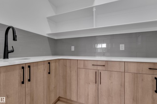 Wood-finish cabinetry with matte black hardware, white countertops, gray subway tile backsplash, and a black gooseneck faucet with an undermount sink - 178 Munn Way, Leduc, AB 