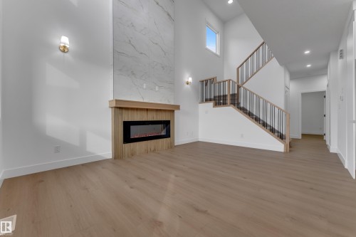 Two-story living area featuring a wood-finish electric fireplace with a floor-to-ceiling marble-look surround, light wood-finish flooring, and recessed lighting - 178 Munn Way, Leduc, AB 