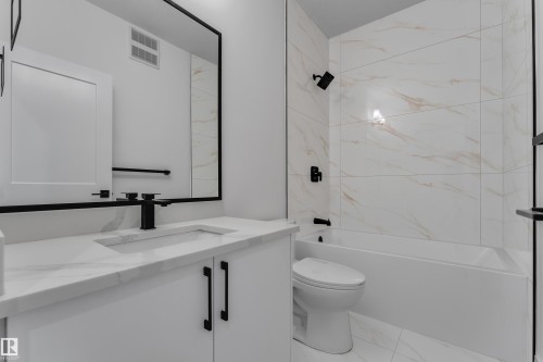 Bathroom featuring a white vanity with an integrated sink, matte black fixtures, a rectangular mirror, and a bathtub with tile surround - 178 Munn Way, Leduc, AB 